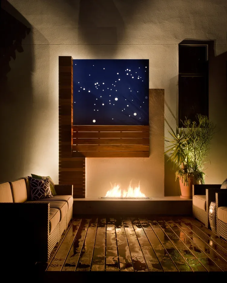Patio with gas fire feature, decorative blue panel with circular cutouts, and wicker seating at night.