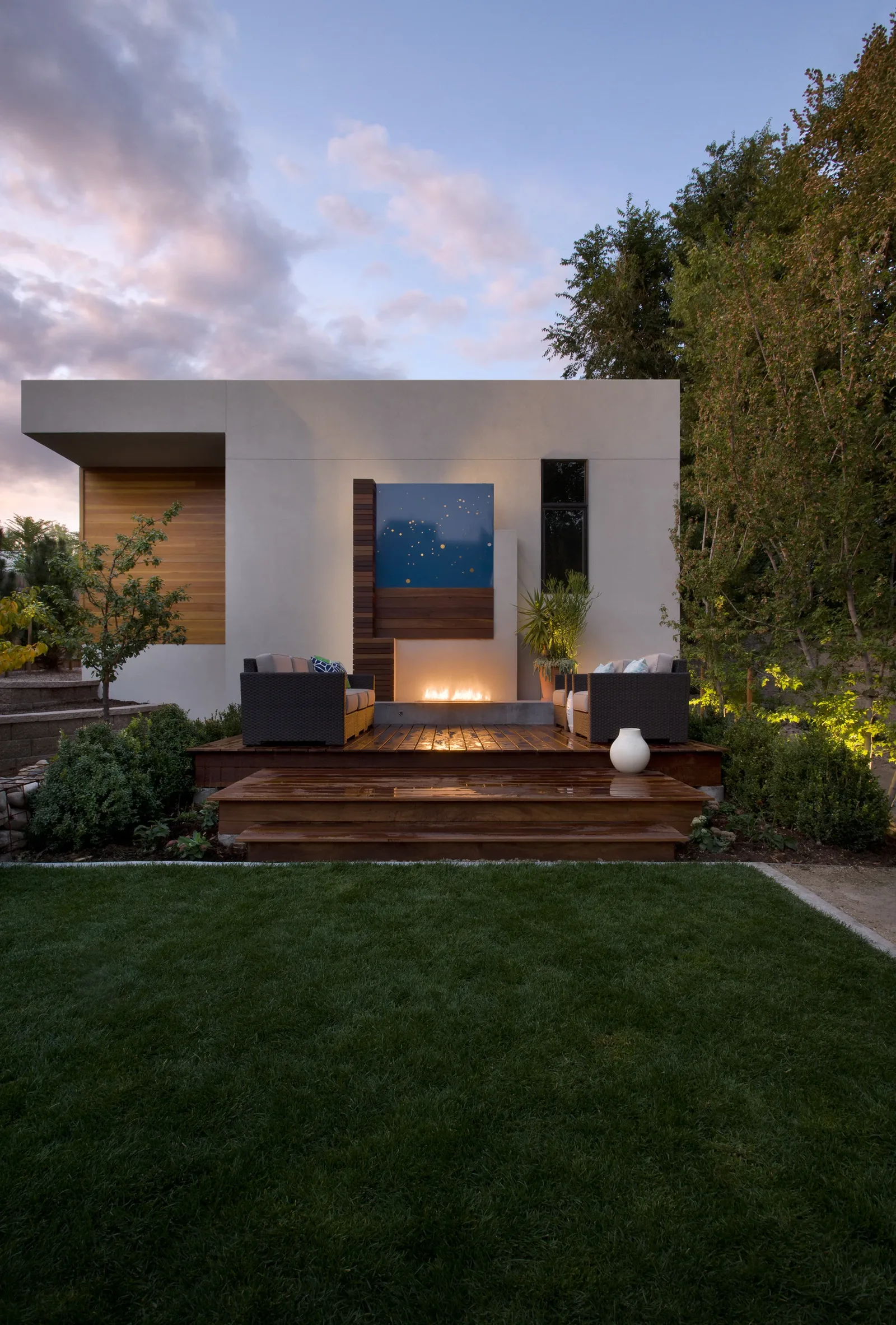 Backyard patio area with wood decking, seating, and a contemporary fireplace feature on a flat-roof structure.