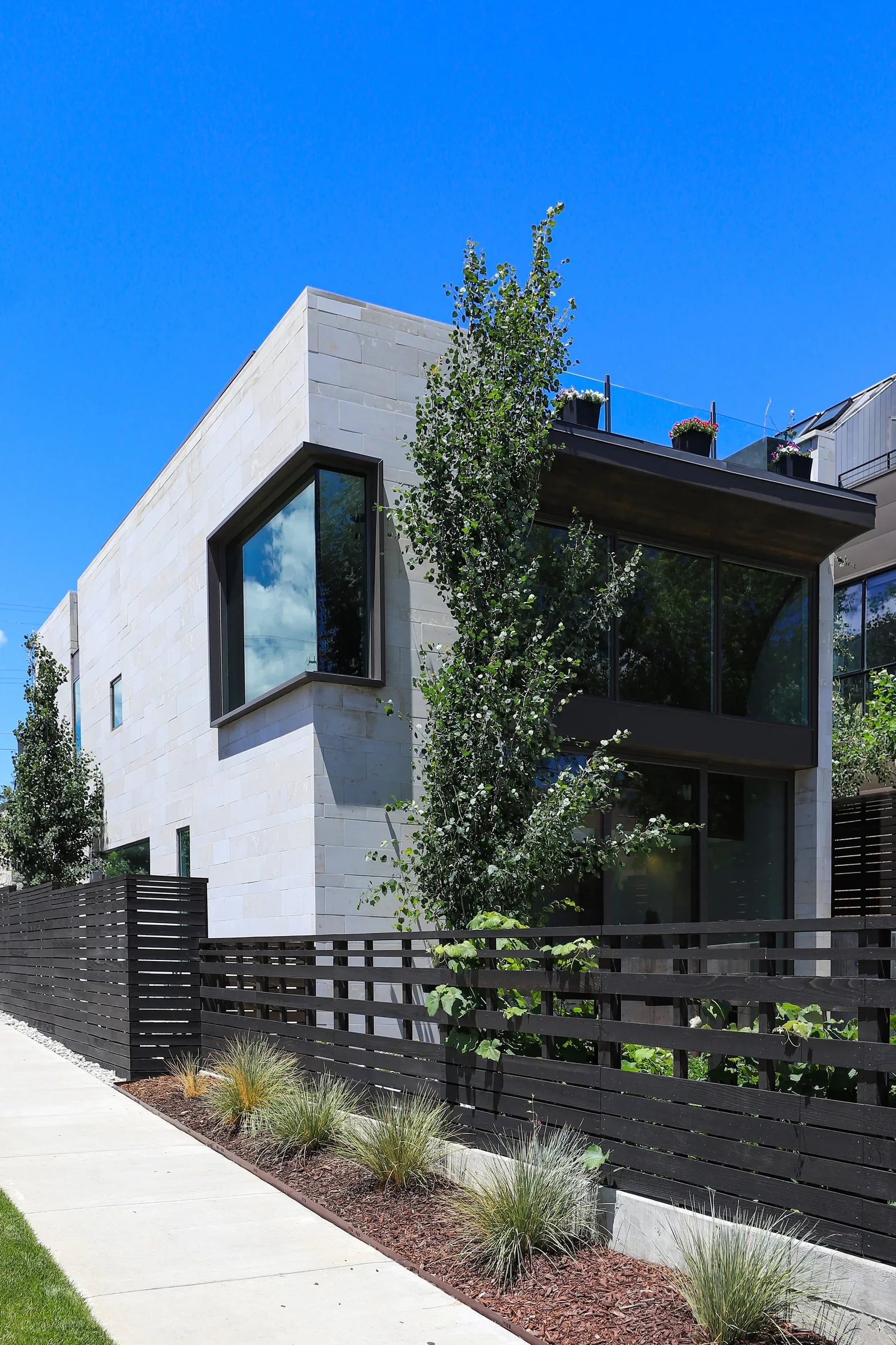 Exterior view of Shoshone Residence featuring light stone cladding, large corner window, and rooftop glass railing.