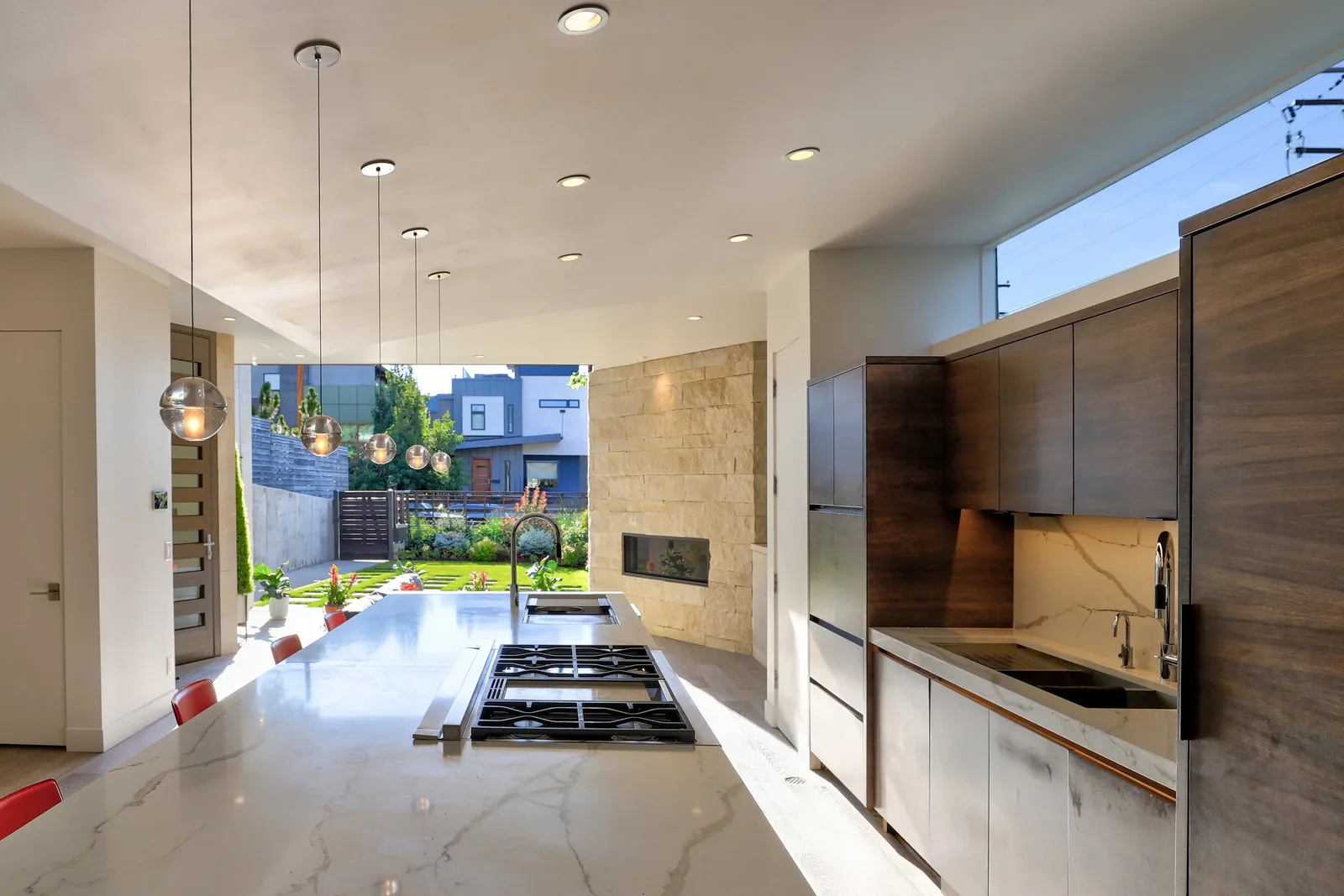 Kitchen with marble island, wood cabinetry, pendant lighting, and a garden view at Shoshone Residence.