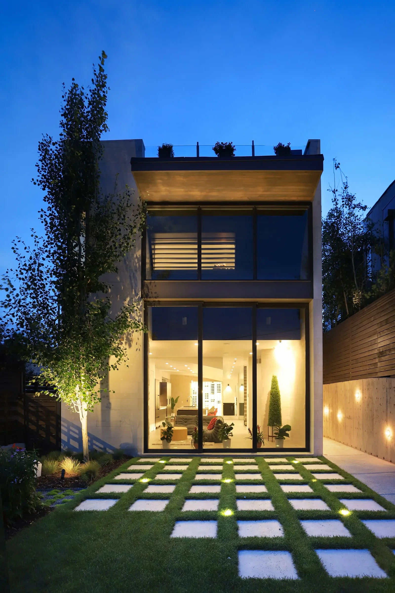 Exterior rear view of Shoshone Residence showing illuminated lawn pavers and expansive glazing.