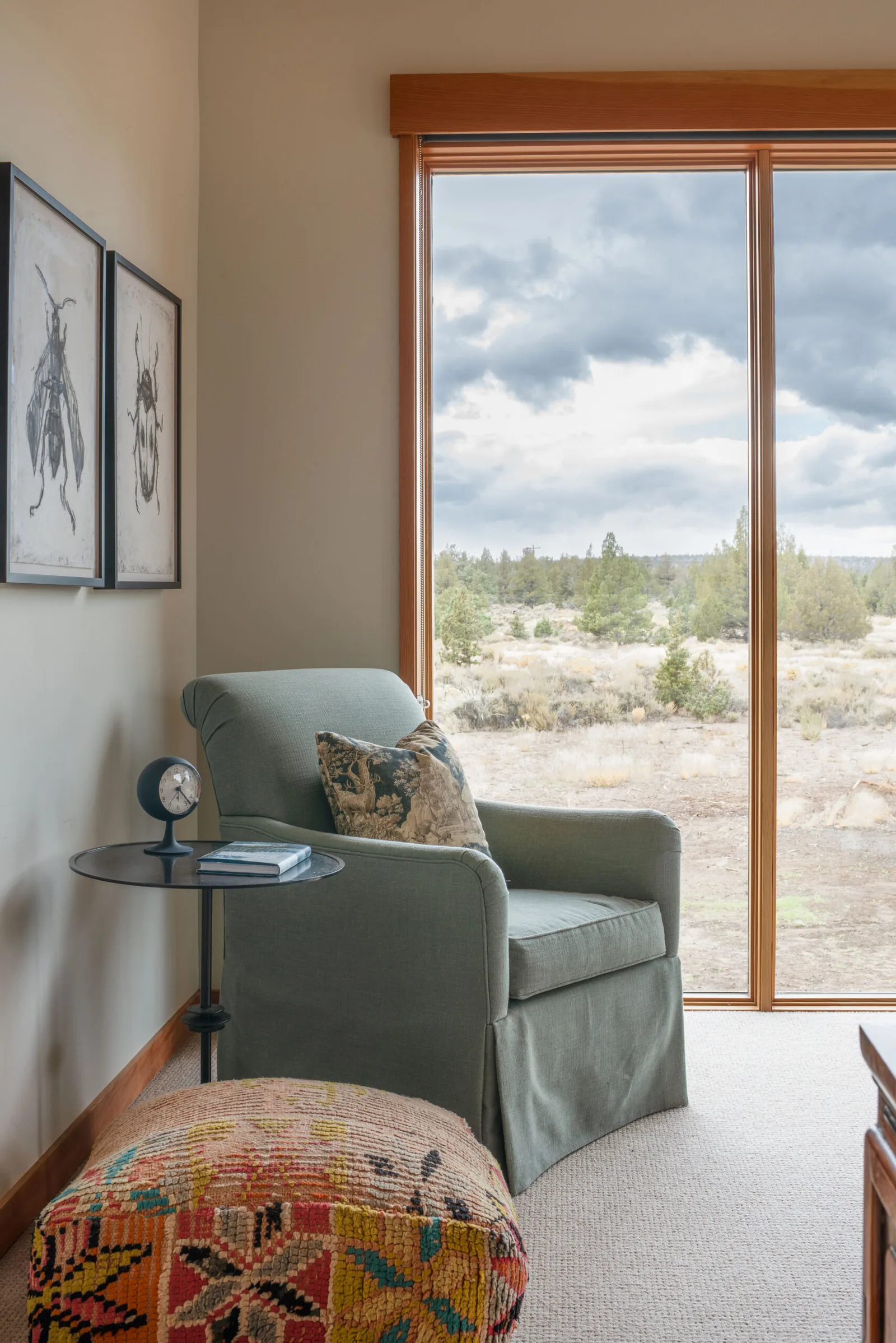 Seating nook with a green armchair and side table beside a large window with desert landscape views.