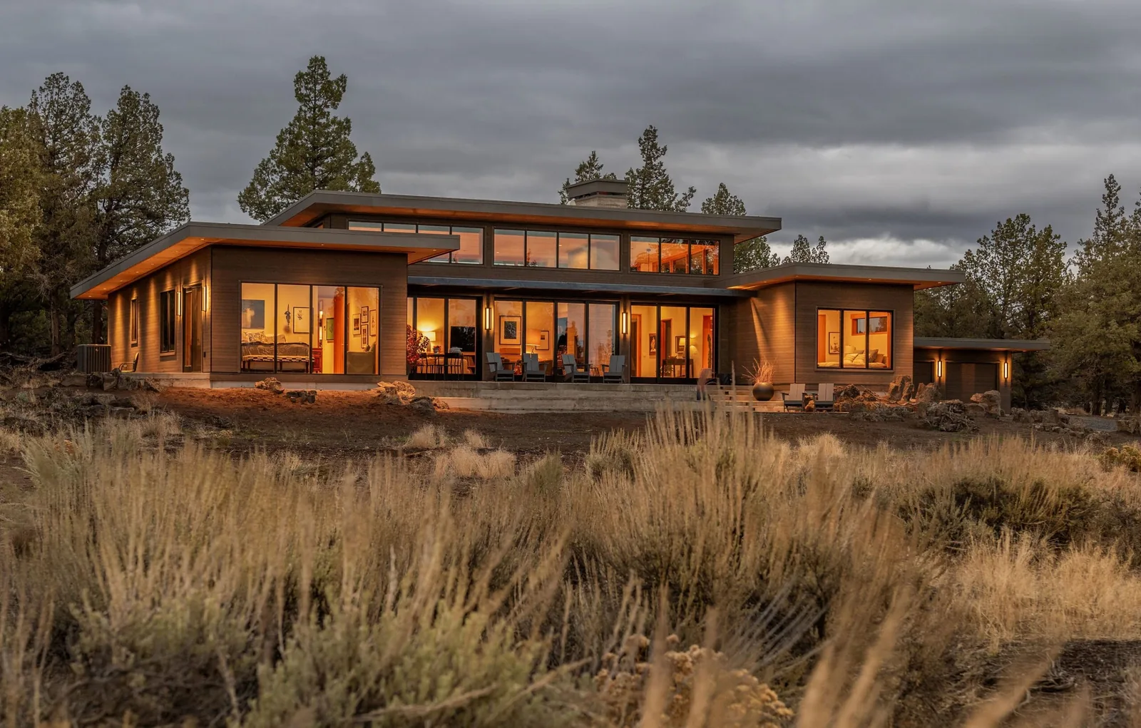 DESCHUTES MODERN OASIS by Emerick Architects features a flat roof and extensive glazing with wood siding in a natural landscape.