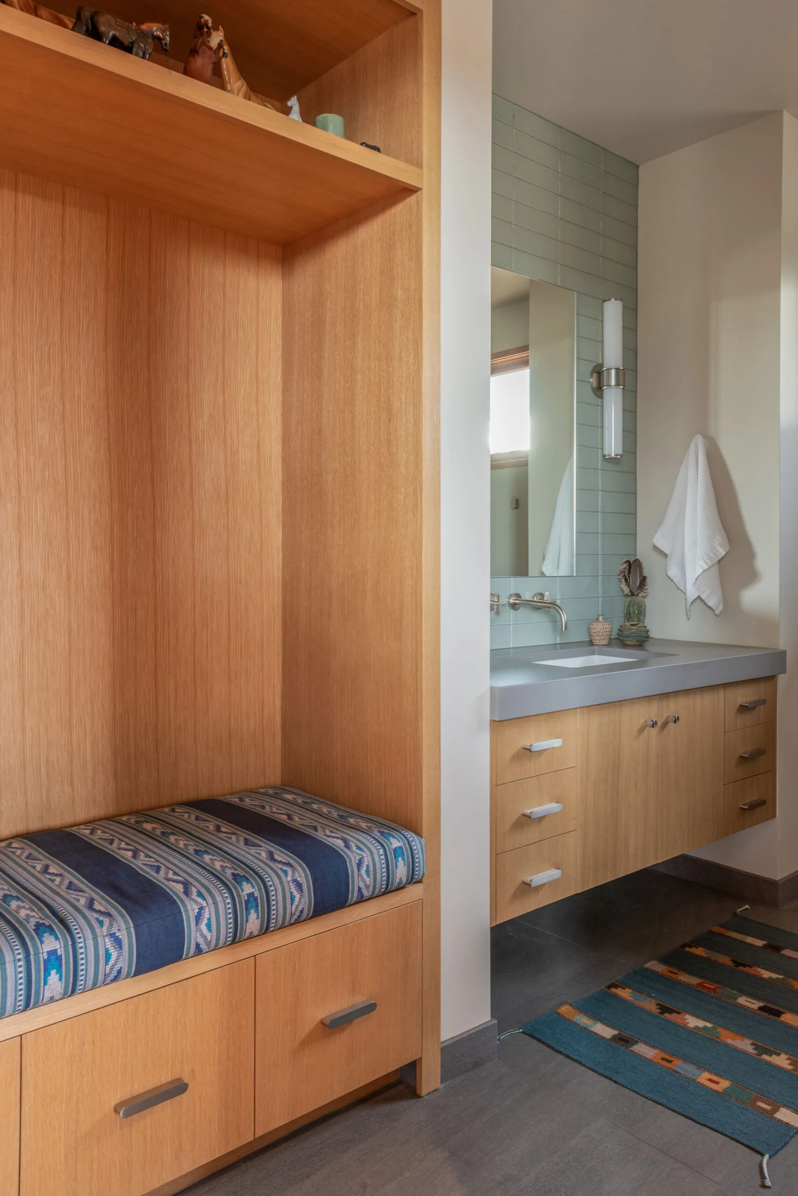 Wood-paneled built-in bench next to a bathroom vanity with light blue tile and a wall-mounted faucet.