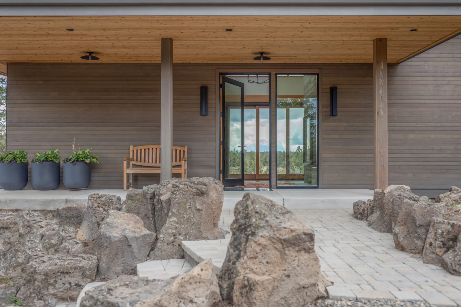 Entry porch of Deschutes Modern Oasis with wood siding and a clear glass pivot door opening to interior.