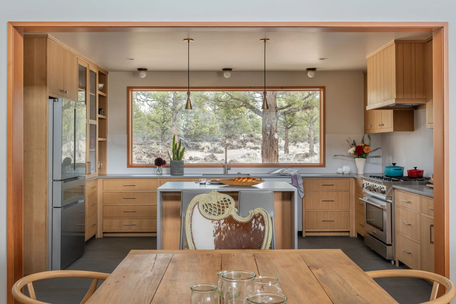 The kitchen features wood cabinets, stainless steel appliances, and a large window with a forest view.
