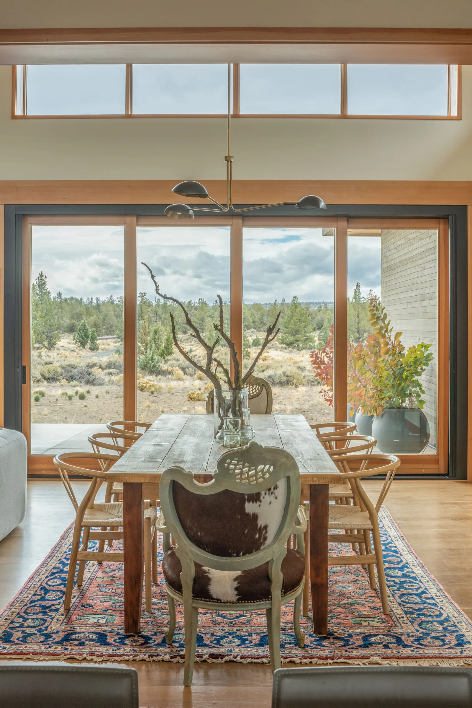 Dining space featuring a natural wood table, diverse seating, and floor-to-ceiling sliding glass doors with scenic views.