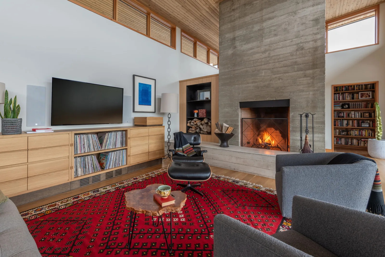 The living room features a concrete fireplace, wood ceiling planks, and a red patterned rug.