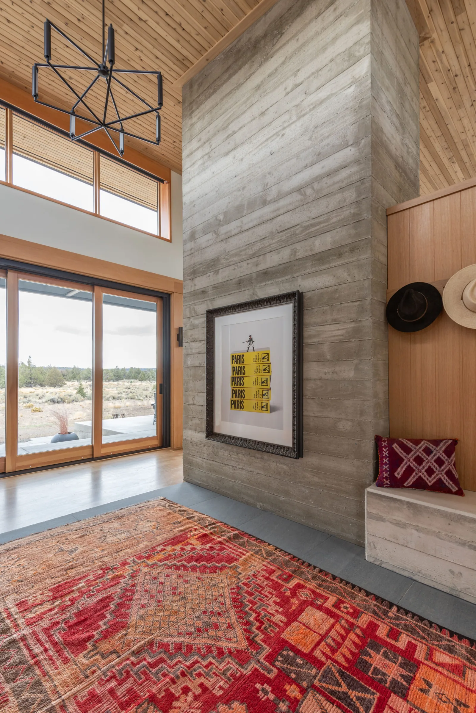 Interior view of entry foyer featuring a concrete accent wall, wood plank ceiling, and a red patterned rug with desert views through sliding glass doors.