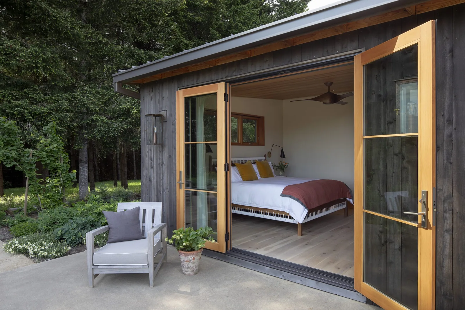Patio view into a bedroom with wide wooden-framed glass doors open to an outdoor seating area.