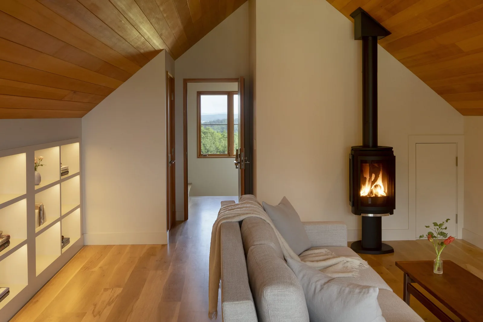 Living room area with built-in shelving and a suspended wood stove under a sloped wooden ceiling.