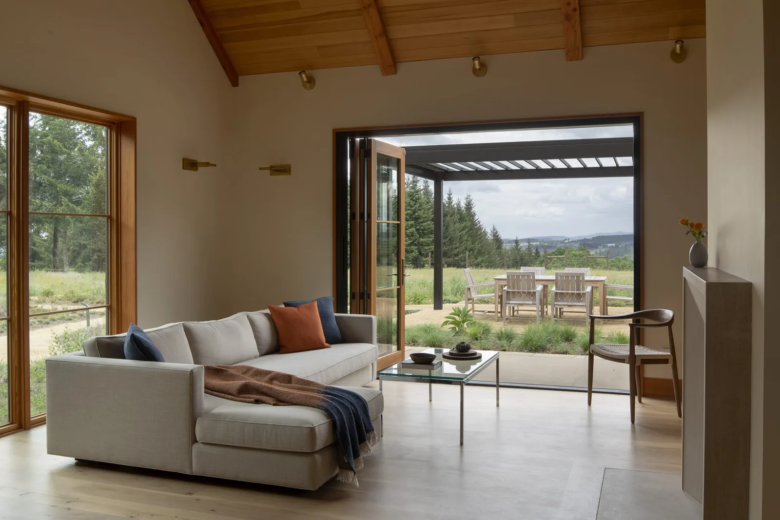 Living room with folding glass doors opens to an outdoor patio with pergola and dining table.