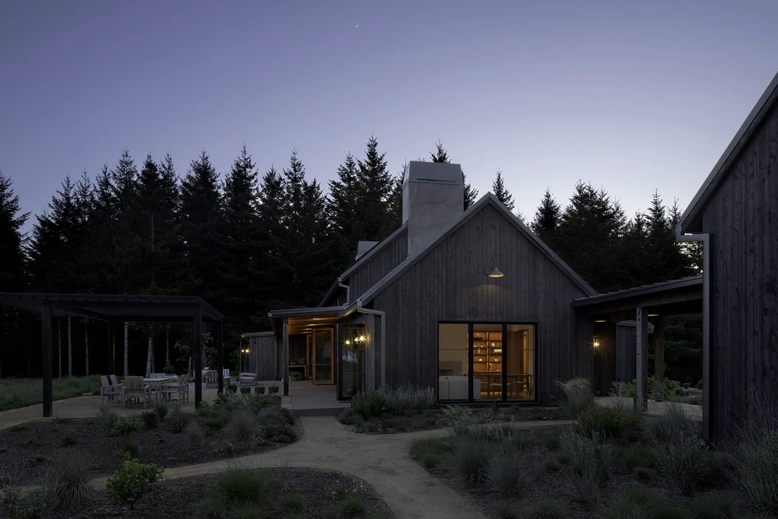 Dusk exterior of a wooden vineyard building with outdoor seating and pathways.