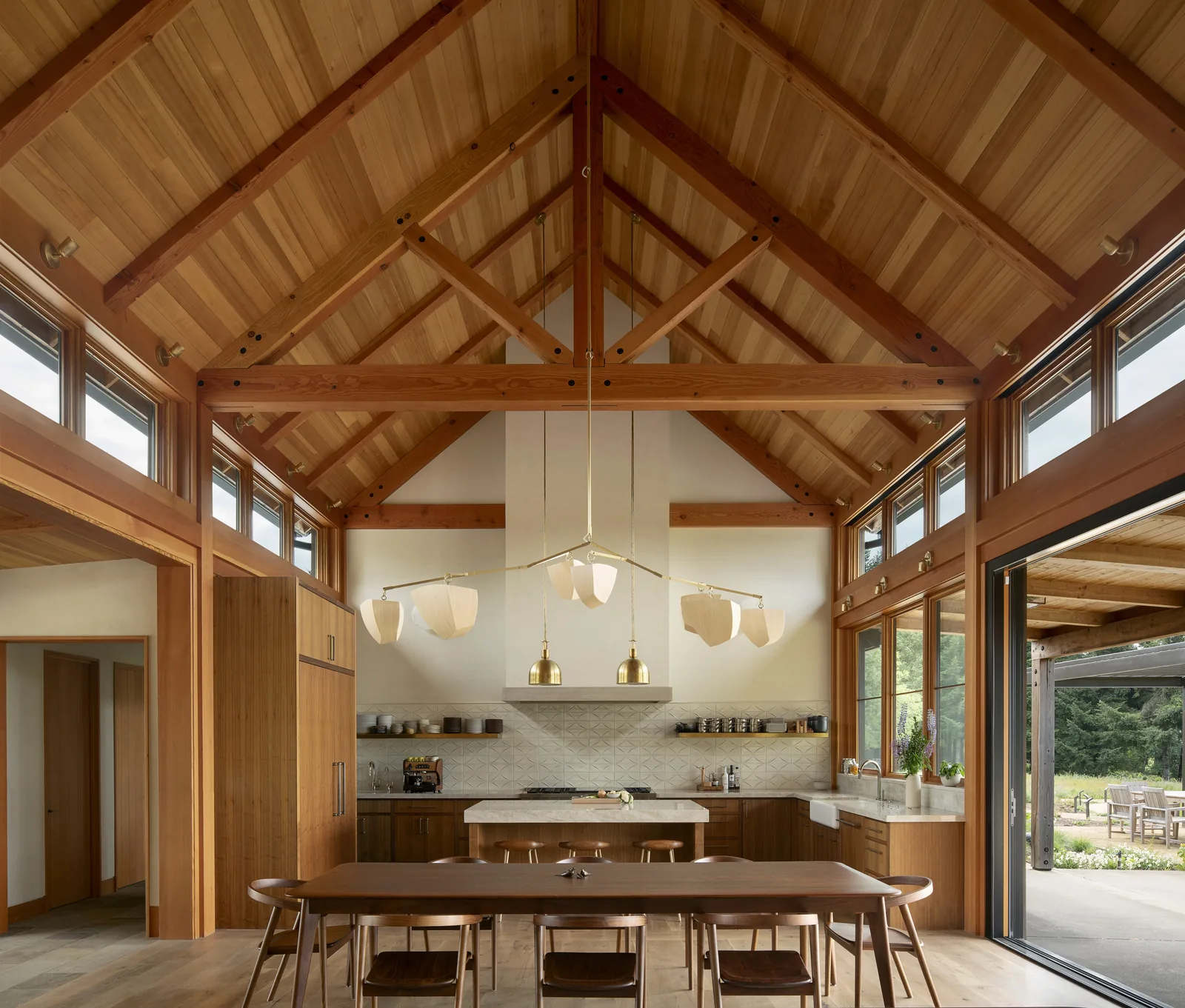 Kitchen and dining area featuring a vaulted ceiling with exposed beams and clerestory windows, adjacent to an open sliding glass door leading to a patio.