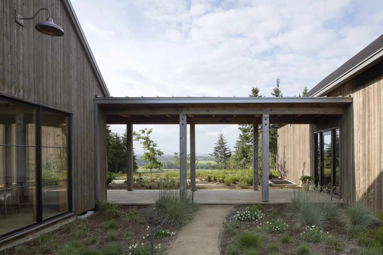 Courtyard connecting two wooden structures with a covered patio and landscape planting at Open Claim Vineyards.