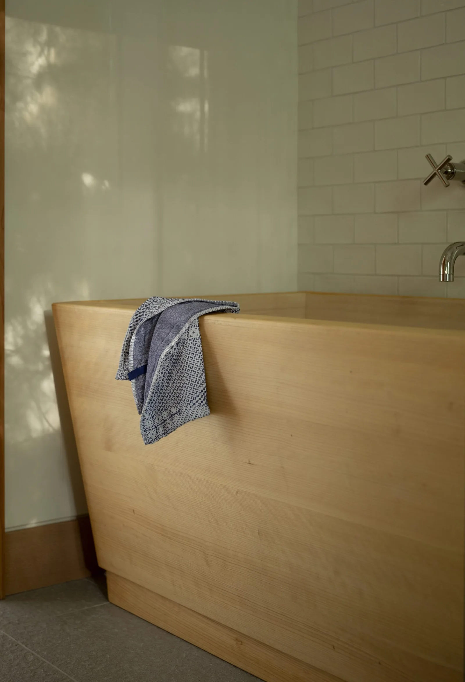 A wooden bathtub with a mounted chrome faucet and towel in a tiled bathroom.
