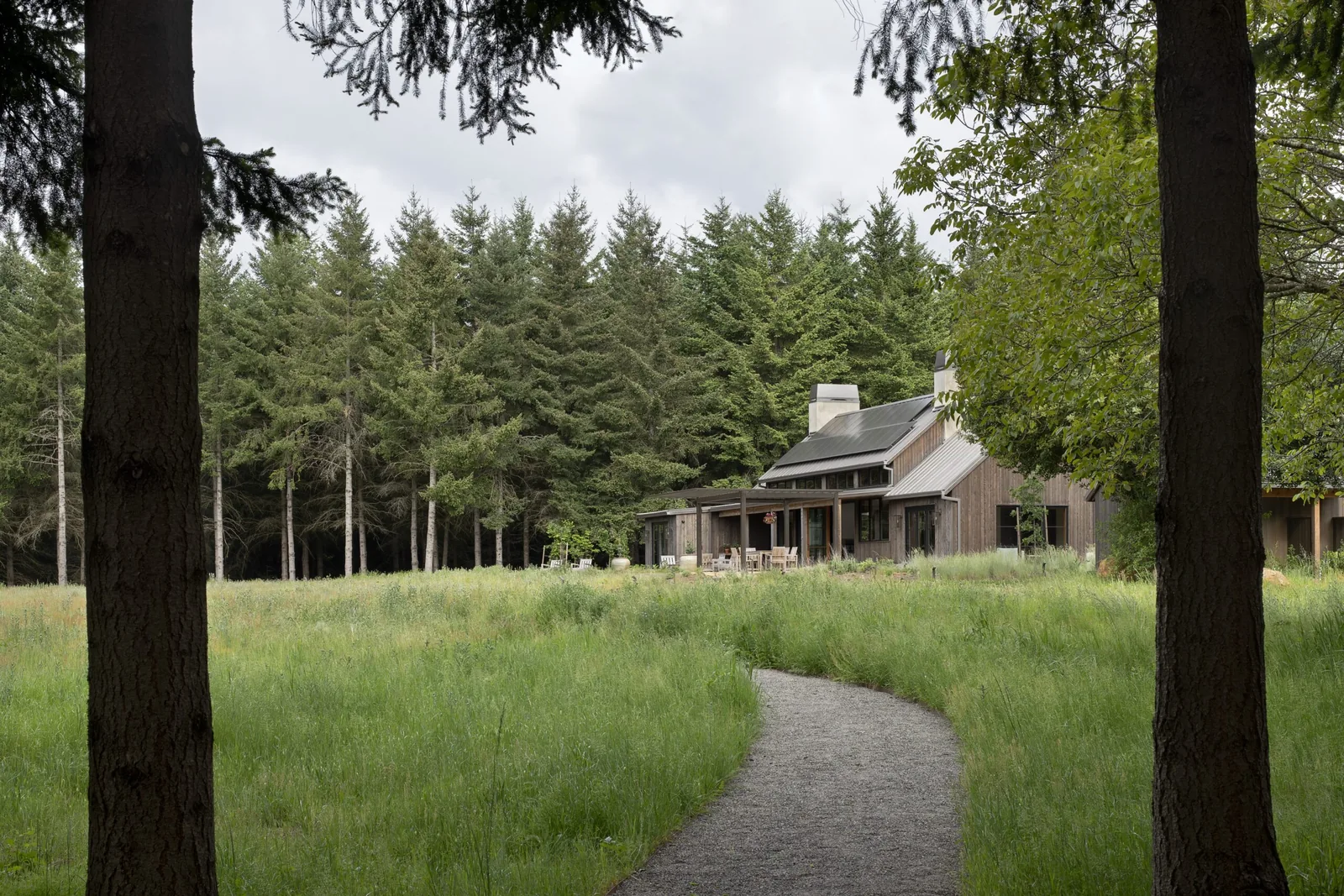 House with a metal roof and wood siding viewed from a gravel path through a grassy field.