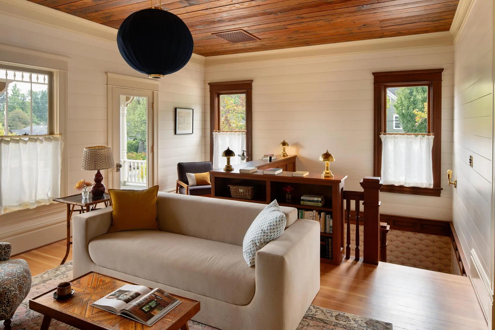 Living room featuring wood ceiling and trim, beige sofa, and stair with built-in bookshelf partition.