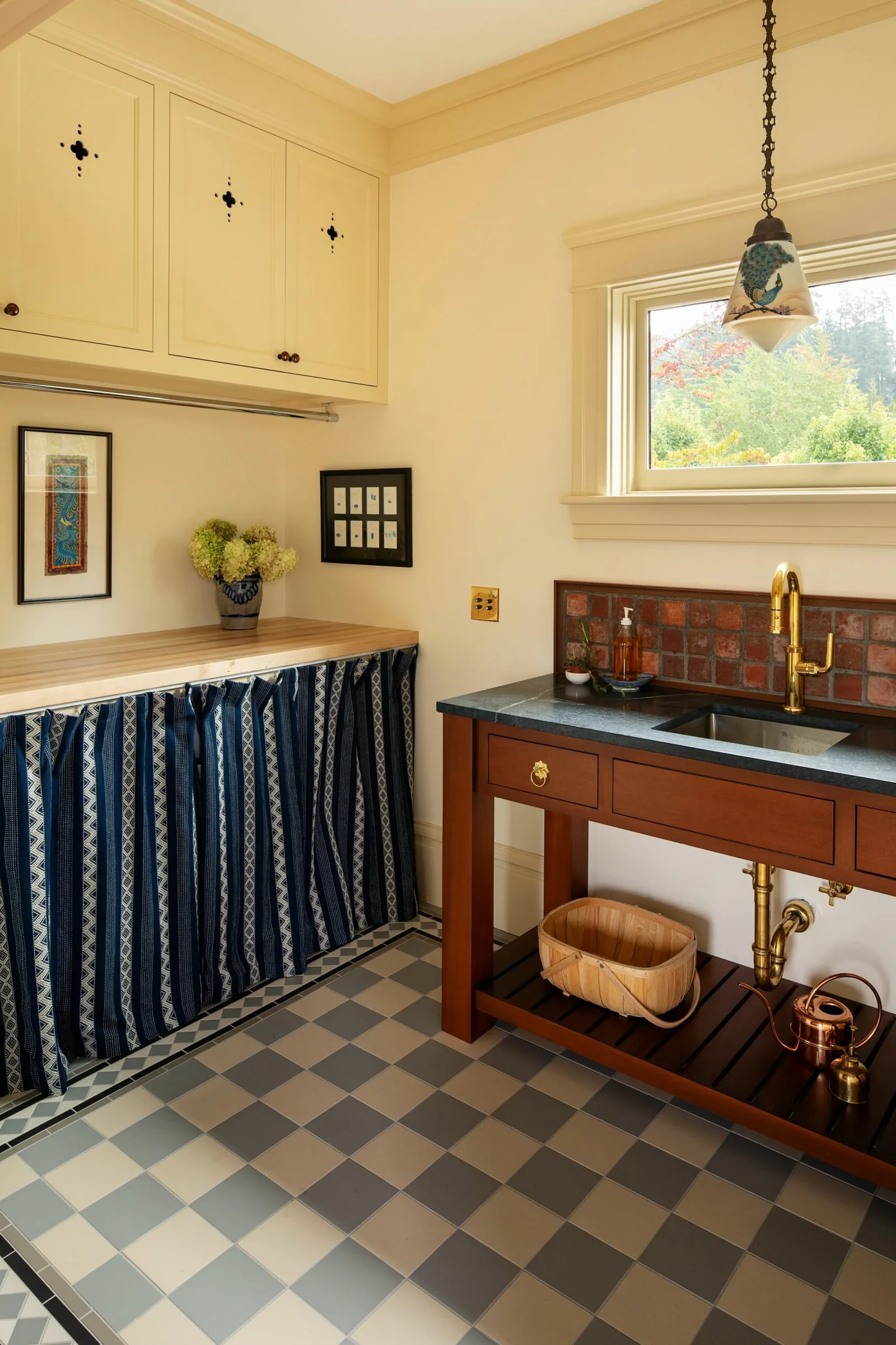 Laundry room featuring a wooden countertop with fabric curtains, cream upper cabinets, and a wood and stone sink unit with brass fixtures.