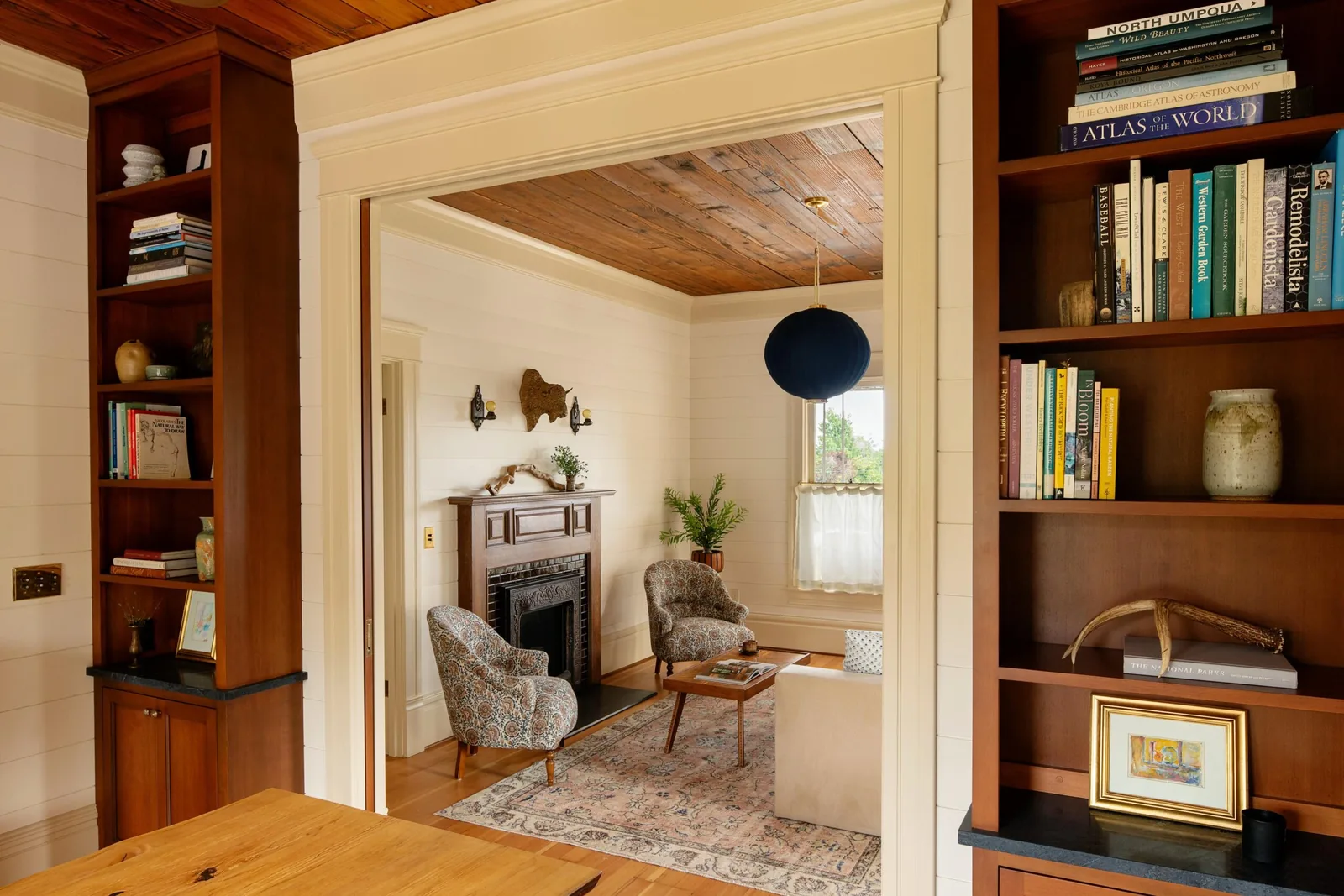 Interior view of a living room with built-in bookshelves, decorative fireplace, and wood-paneled ceiling.
