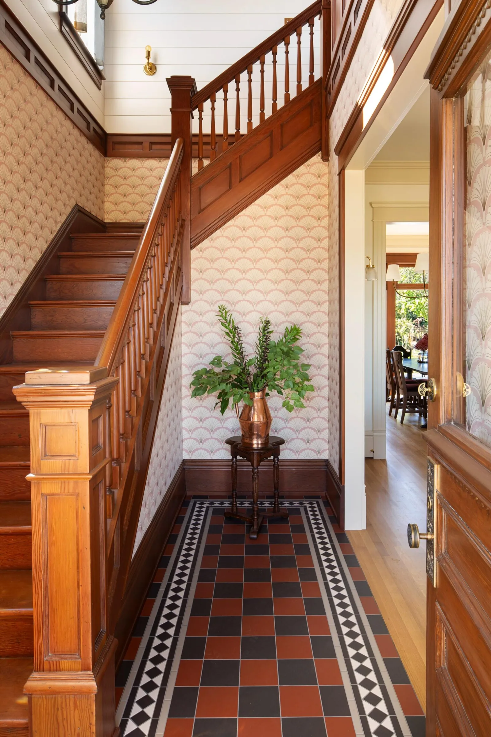 Wooden staircase and entry with patterned tile floor and wallpaper in a traditional style residence.