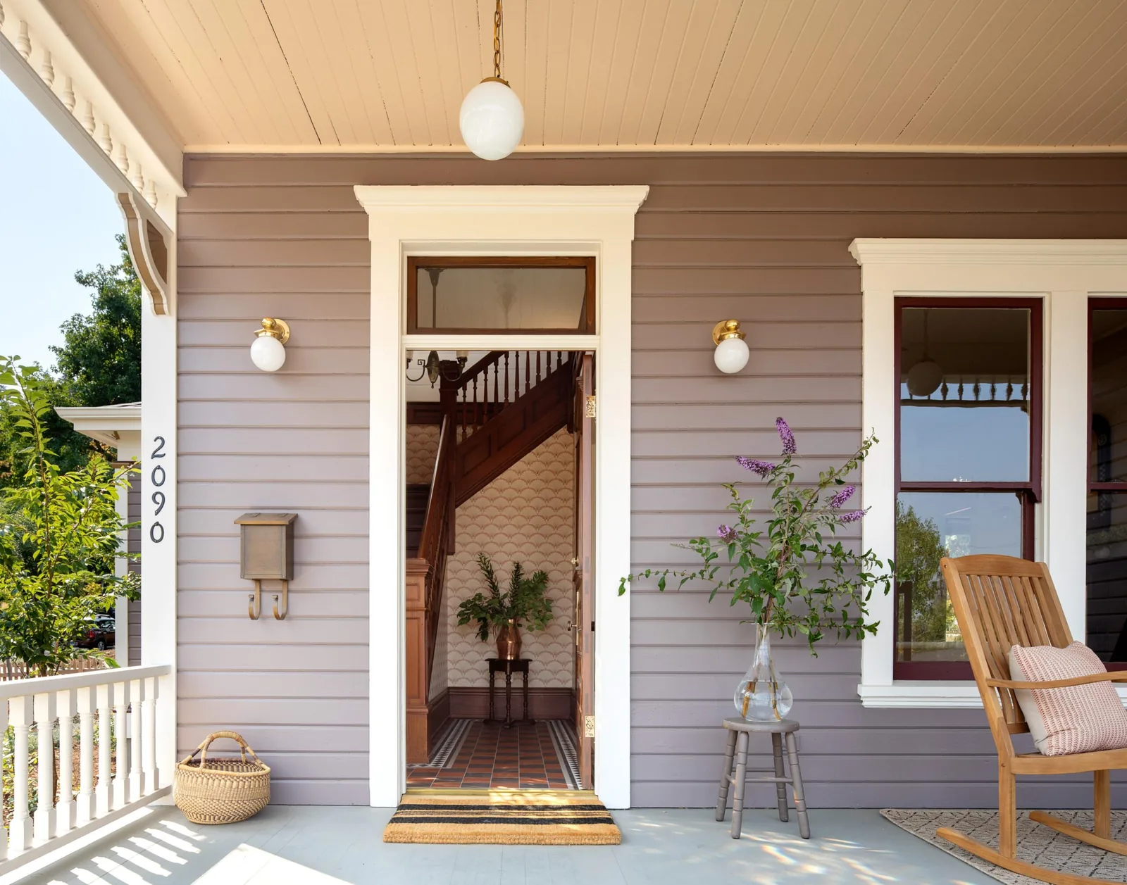 Front porch view showing open door, wooden rocking chair, and exterior wall lighting fixtures.