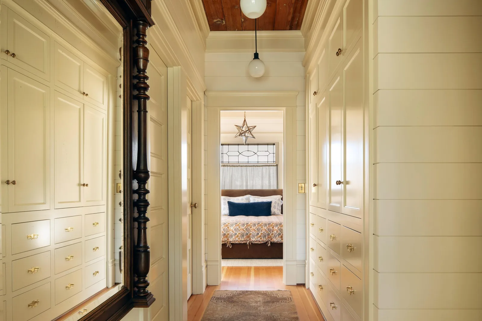 Interior hallway with built-in storage cabinets leads to a bedroom with decorative window and hanging star light fixture.