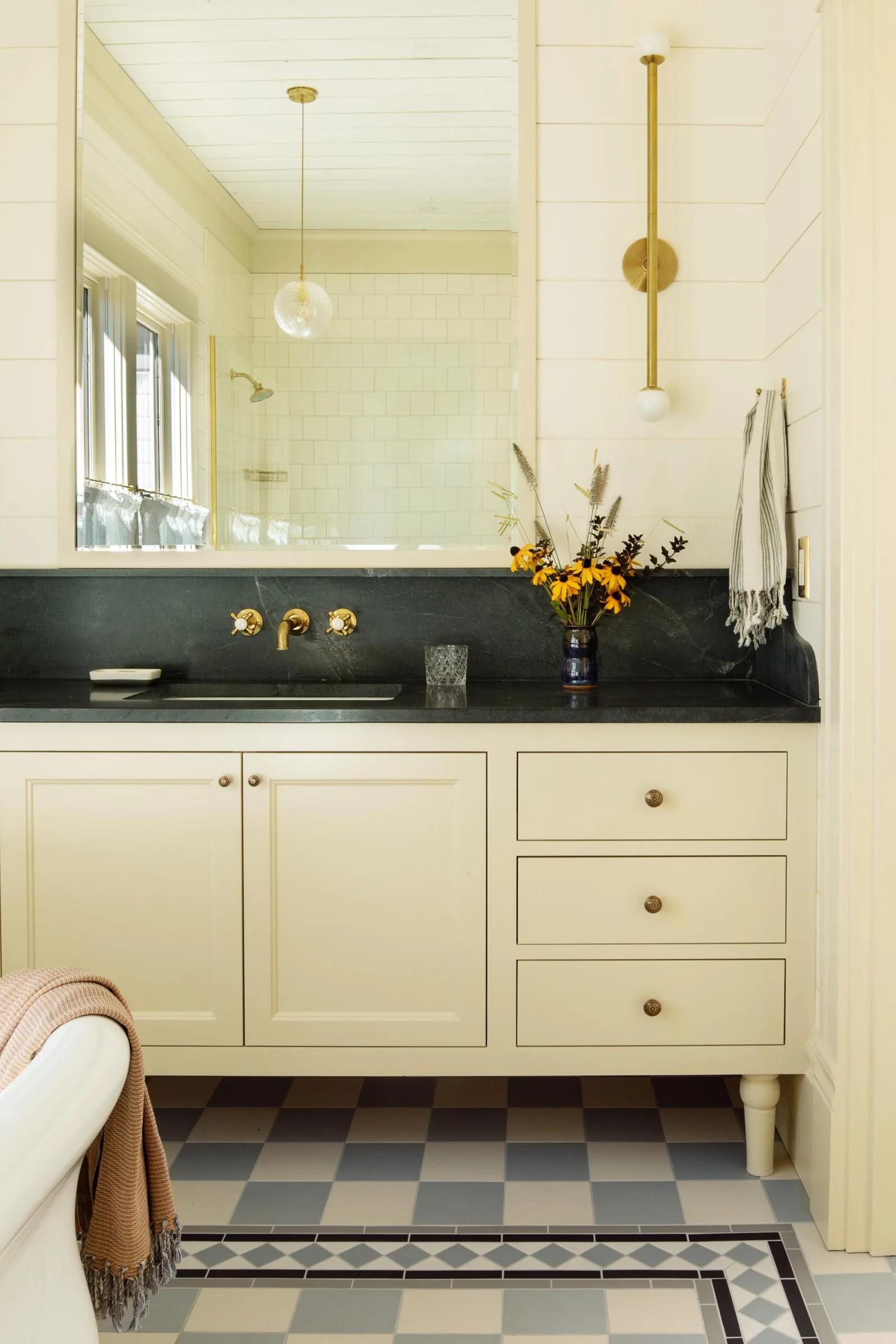Bathroom vanity area with black countertop and cream cabinetry in front of a large mirror.