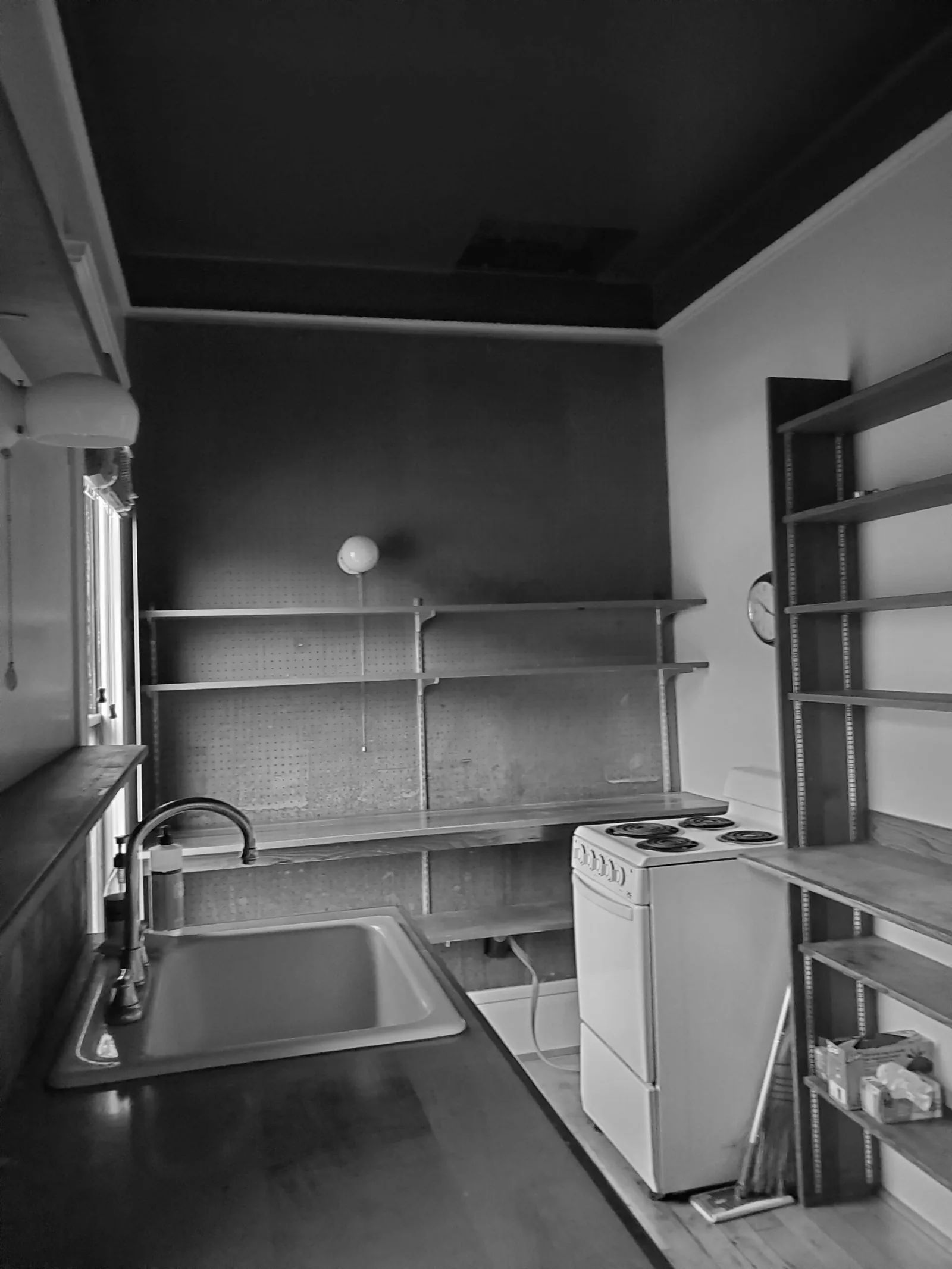 Small kitchen featuring open wood shelves, a stainless faucet over a single-bowl sink, and a compact electric stove.