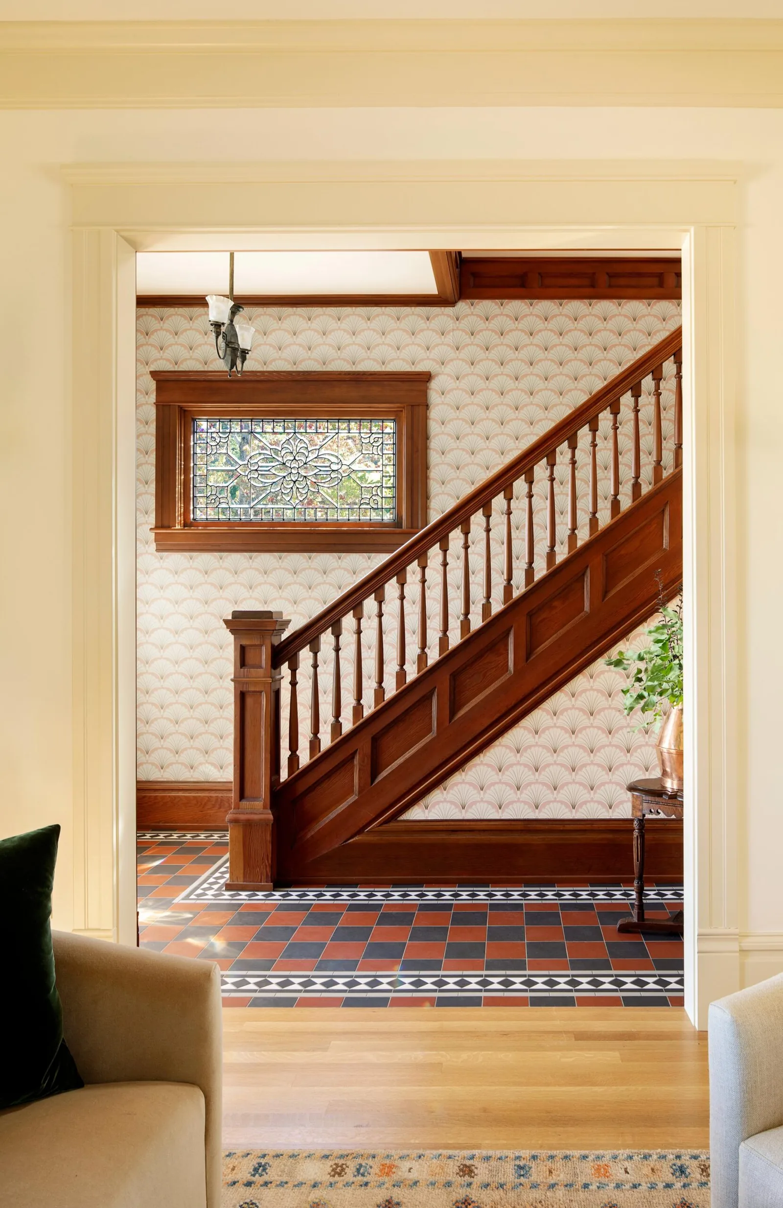 Wooden staircase with patterned tile flooring and a stained glass window in the entry hallway.
