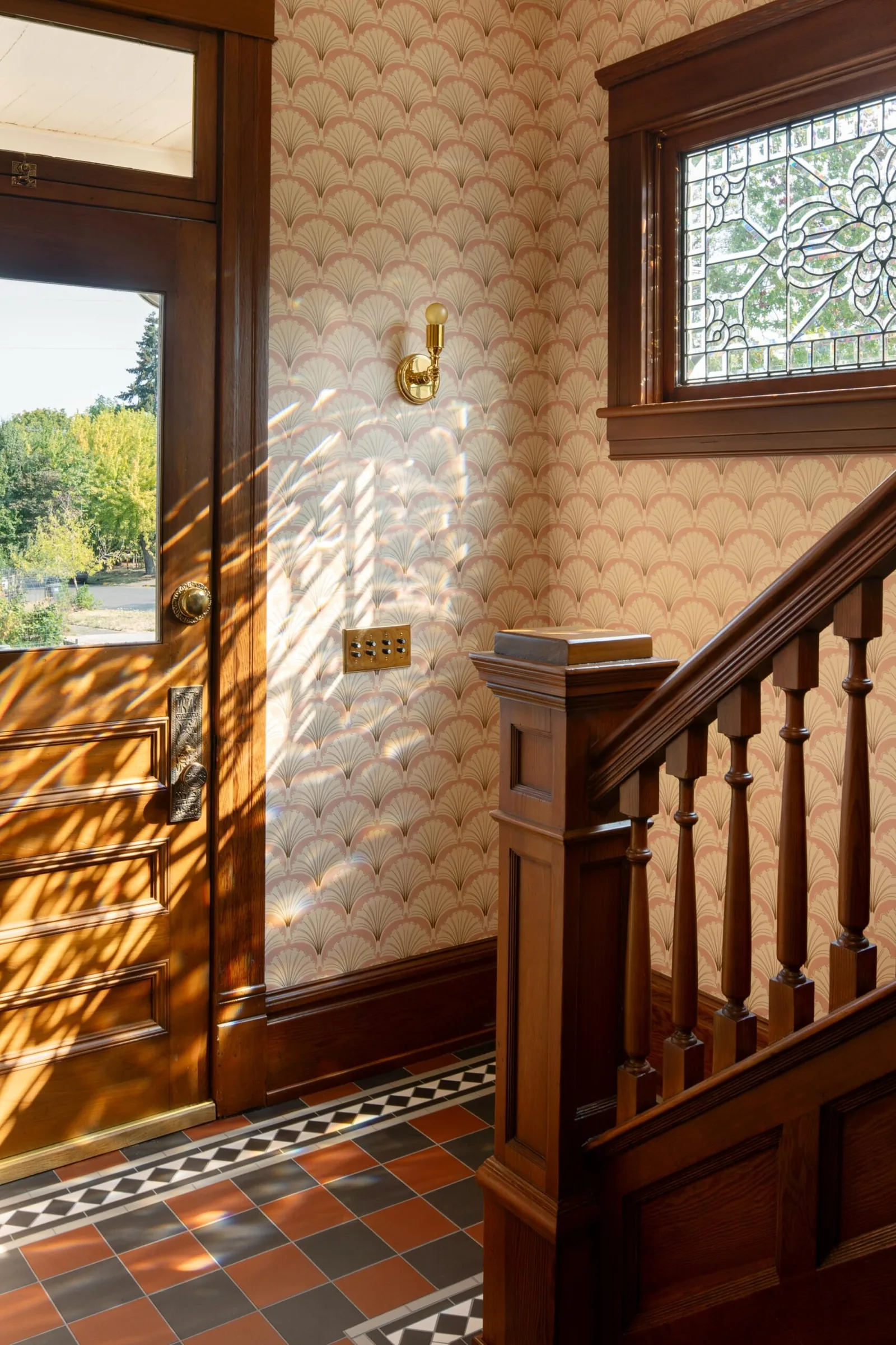 Entryway featuring a wooden door, patterned wallpaper, a stained glass window, and a wooden staircase with balusters.