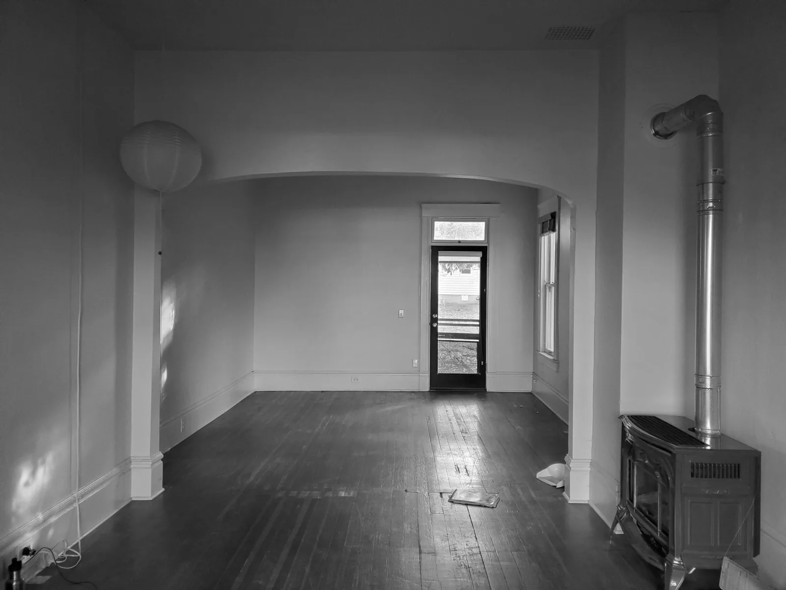 Interior view of an empty room with a wood stove and an archway leading to an exterior door.