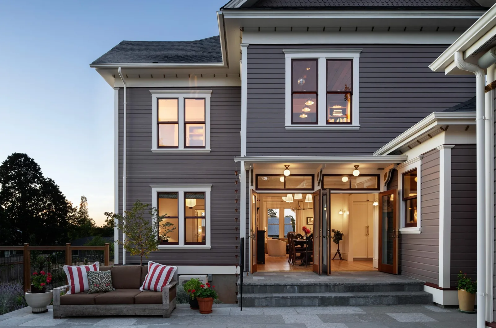 Rear elevation of a two-story Queen Anne style house featuring gray siding, multiple windows with white trim, and an open patio door.