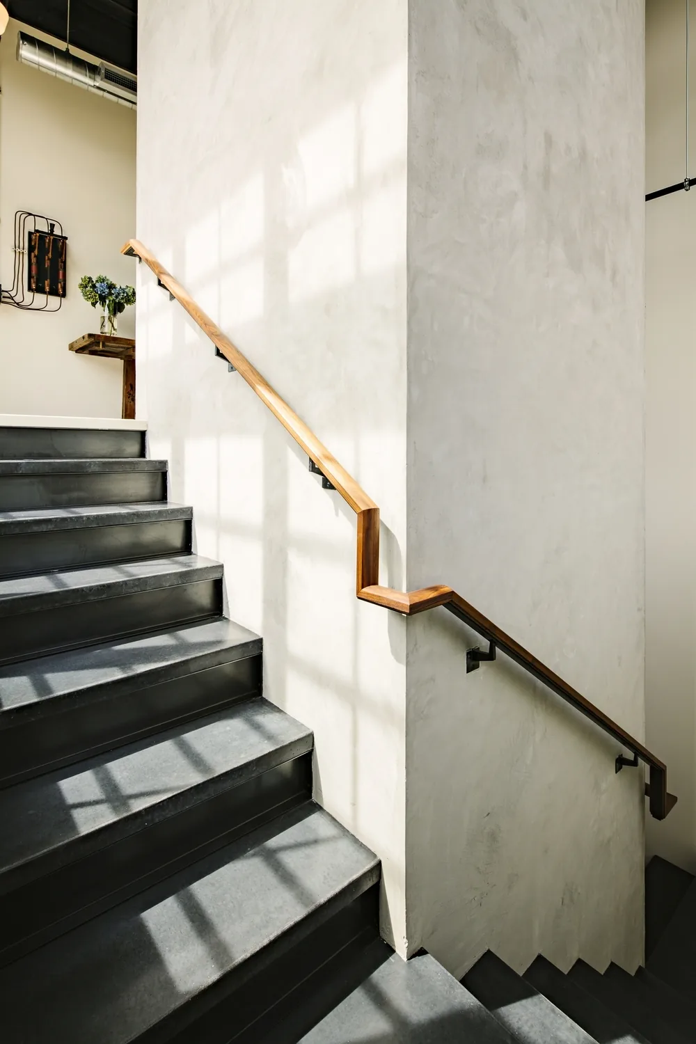 Interior staircase with black metal steps and a wooden handrail in the Division Street Residence.