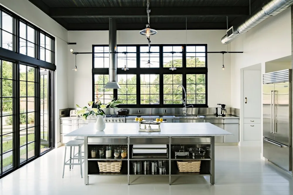 Kitchen with stainless steel appliances and large industrial-style black window frames in Division Street Residence.