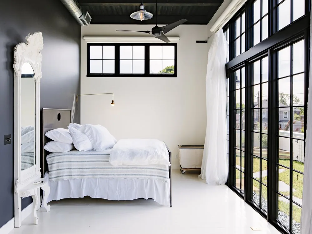 Bedroom in Division Street Residence features black industrial window grids and high ceilings.