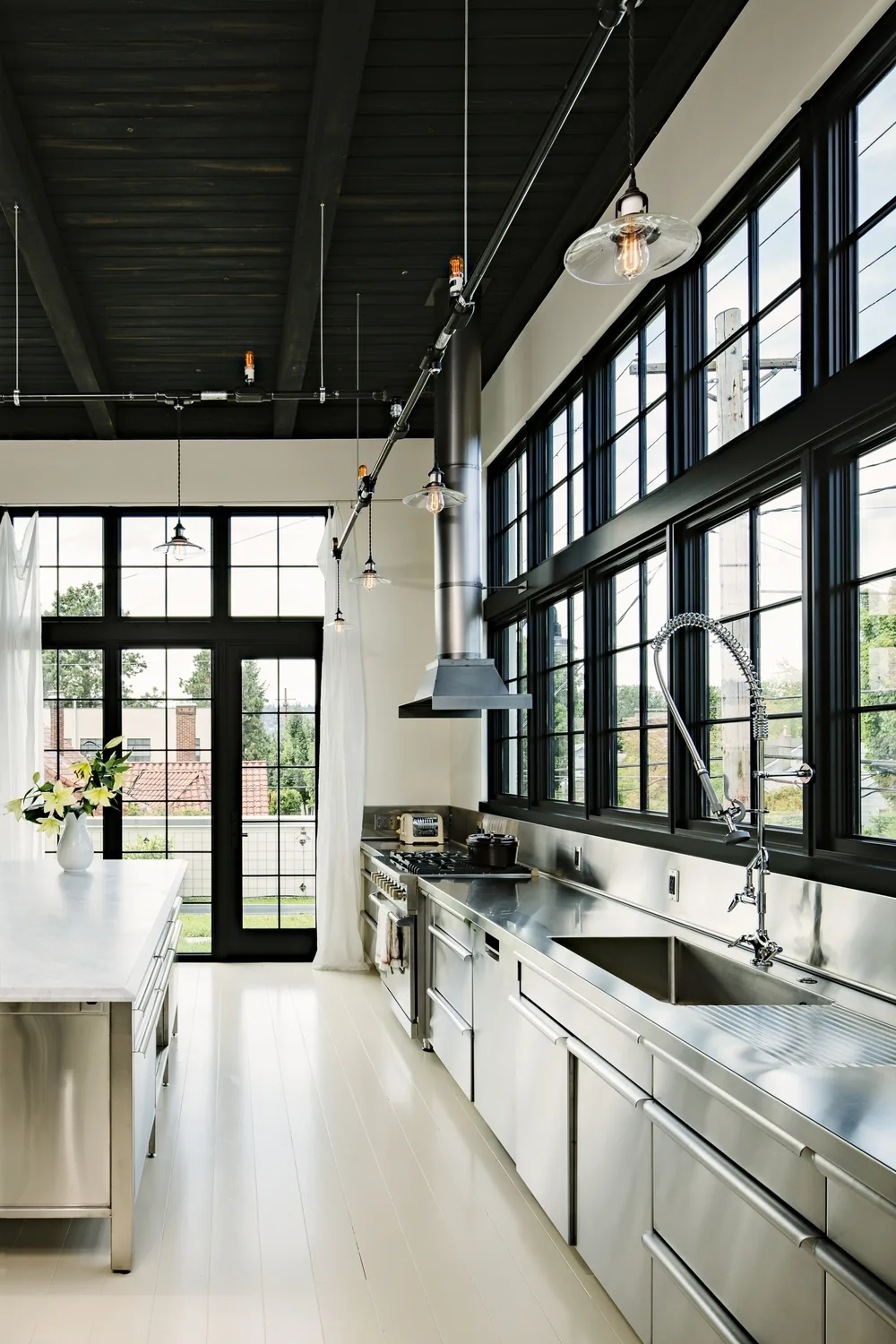 The Division Street Residence kitchen features industrial-style black window grids, stainless steel counters, and pendant lighting by Emerick Architects in Portland.