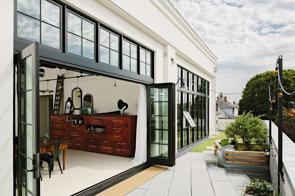 Industrial steel-frame folding doors open onto a patio with raised planters at Division Street Residence.