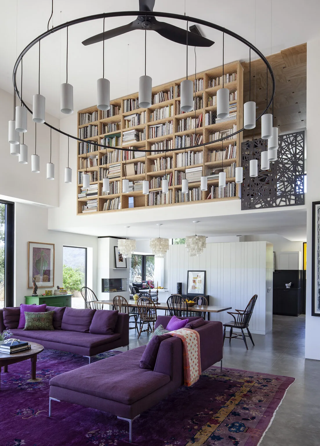 Living and dining area with a large built-in bookshelf, purple sofas, and a circular pendant light fixture.