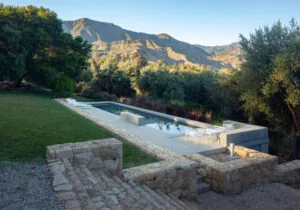 Outdoor rectangular pool with stone retaining walls and mountain backdrop.
