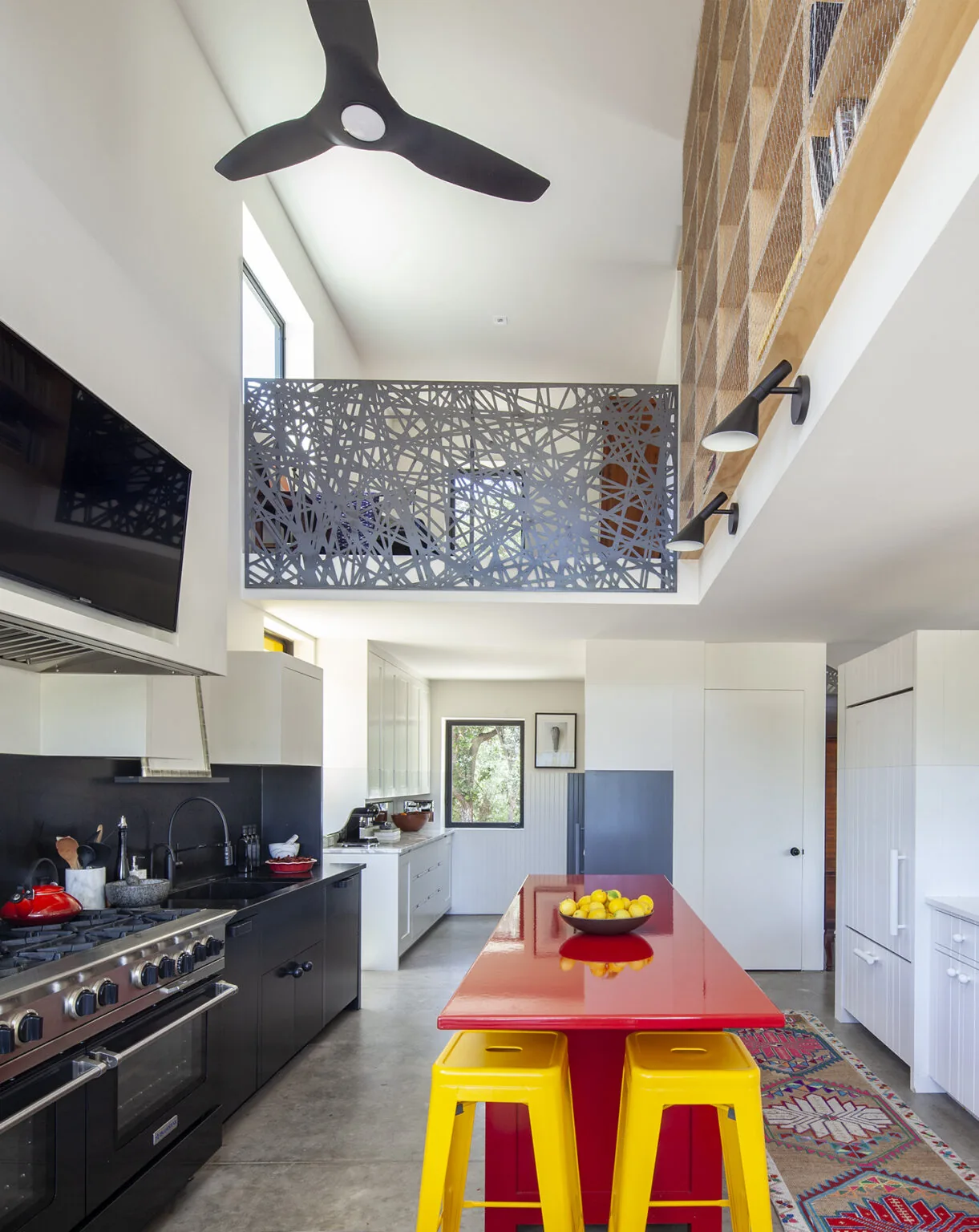 Modern kitchen features a red island with yellow stools and a decorative metal balcony railing above.