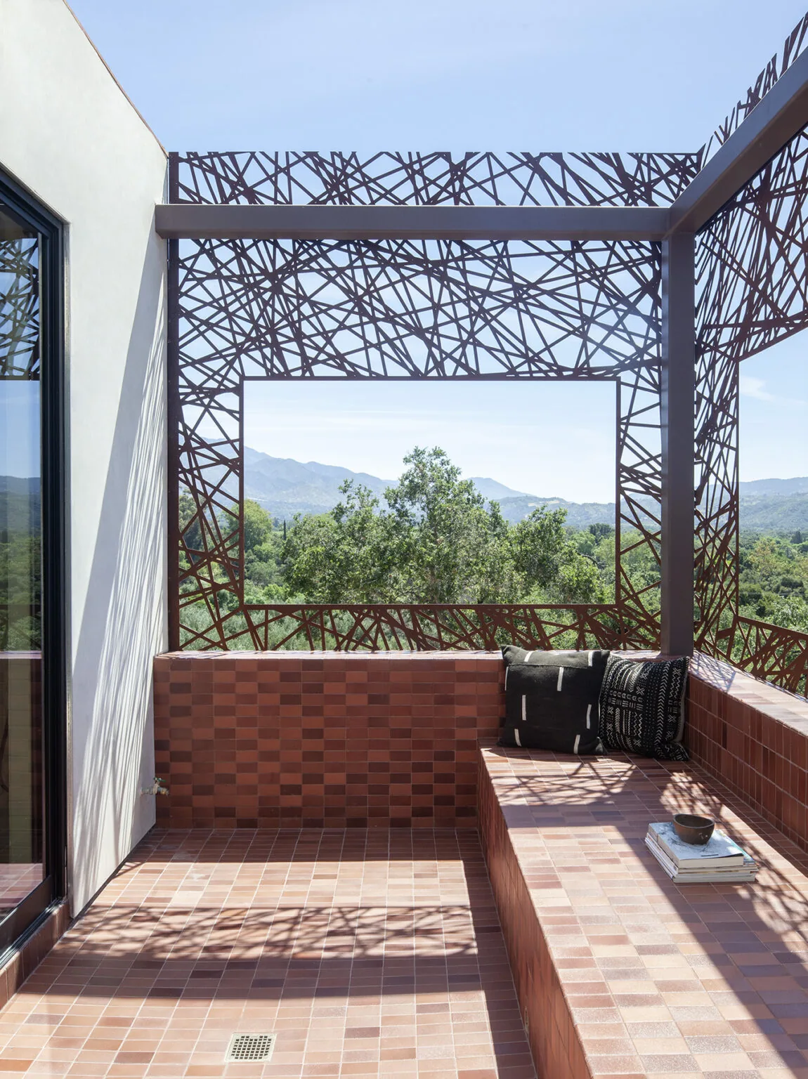 Terrace area with tiled flooring and built-in seating enclosed by an artistic metal screen offering views of natural landscape and mountains.