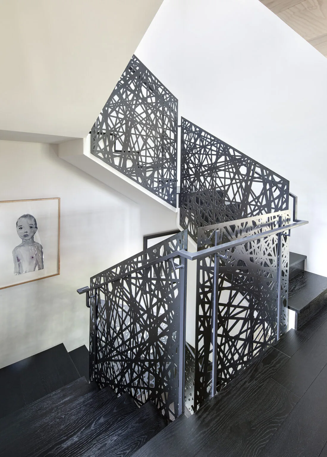 Interior view of a staircase featuring dark wood steps and artistic metal railings with an abstract linear pattern.