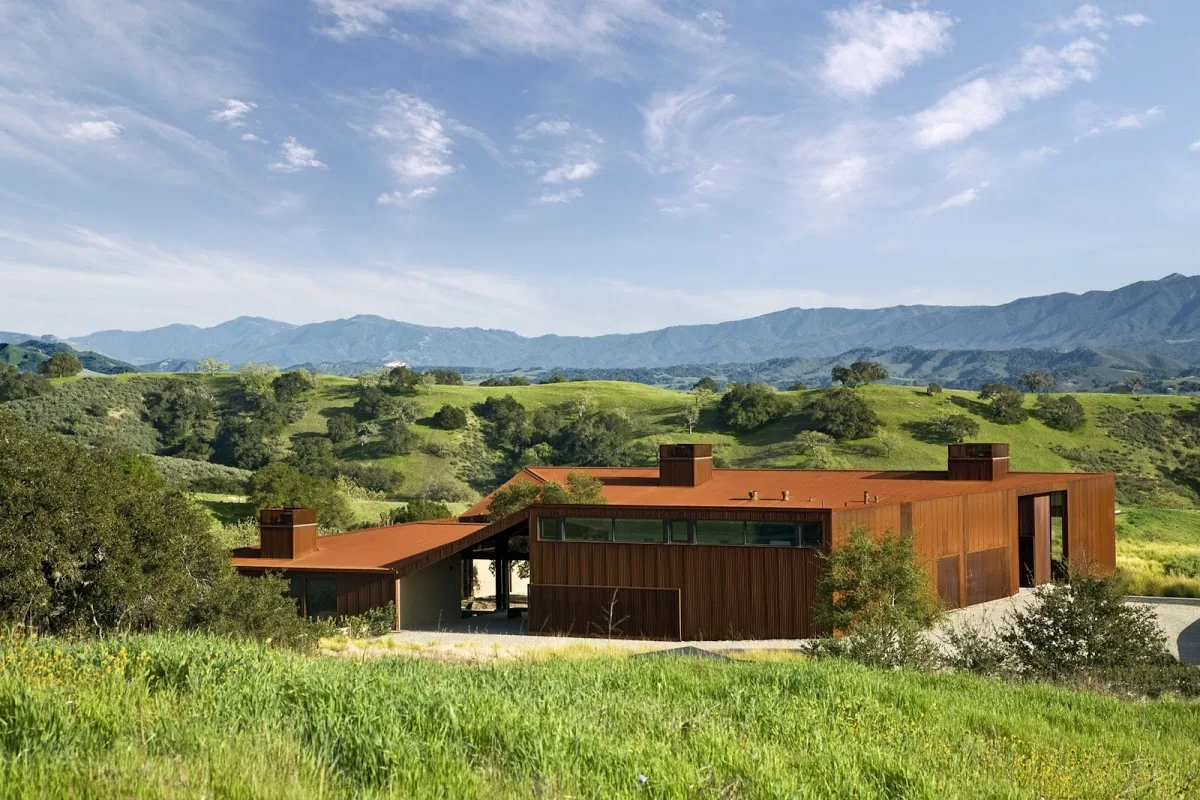 Santa Ynez Residence features a rust-colored flat-roof home nestled in rolling green hills.