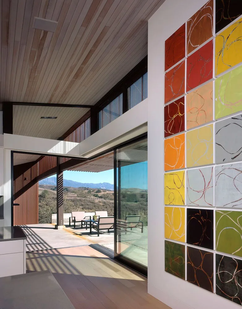 The Santa Ynez Residence features a wood plank ceiling and wide sliding glass doors connecting to the outdoor patio with views of the hillside landscape.