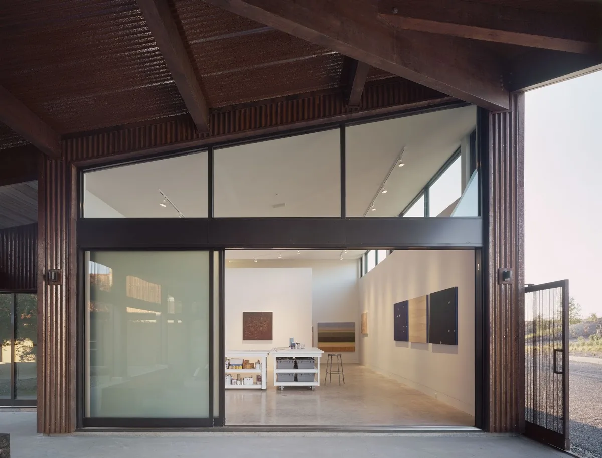 Santa Ynez Residence features an art studio with high ceilings, wide rectangular windows, and a sliding glass door opening to the outdoors.