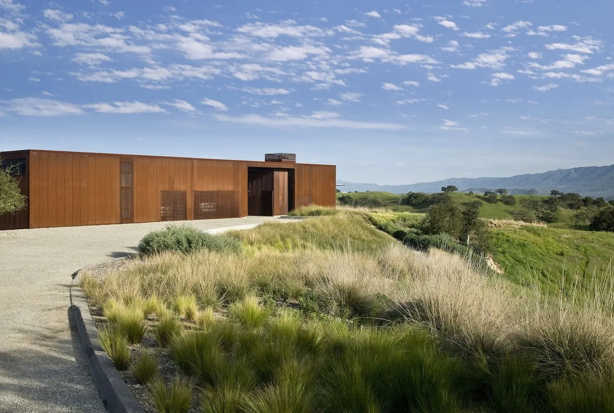 The Santa Ynez Residence features a rust-colored exterior integrated with natural grassy landscaping on a hillside site.