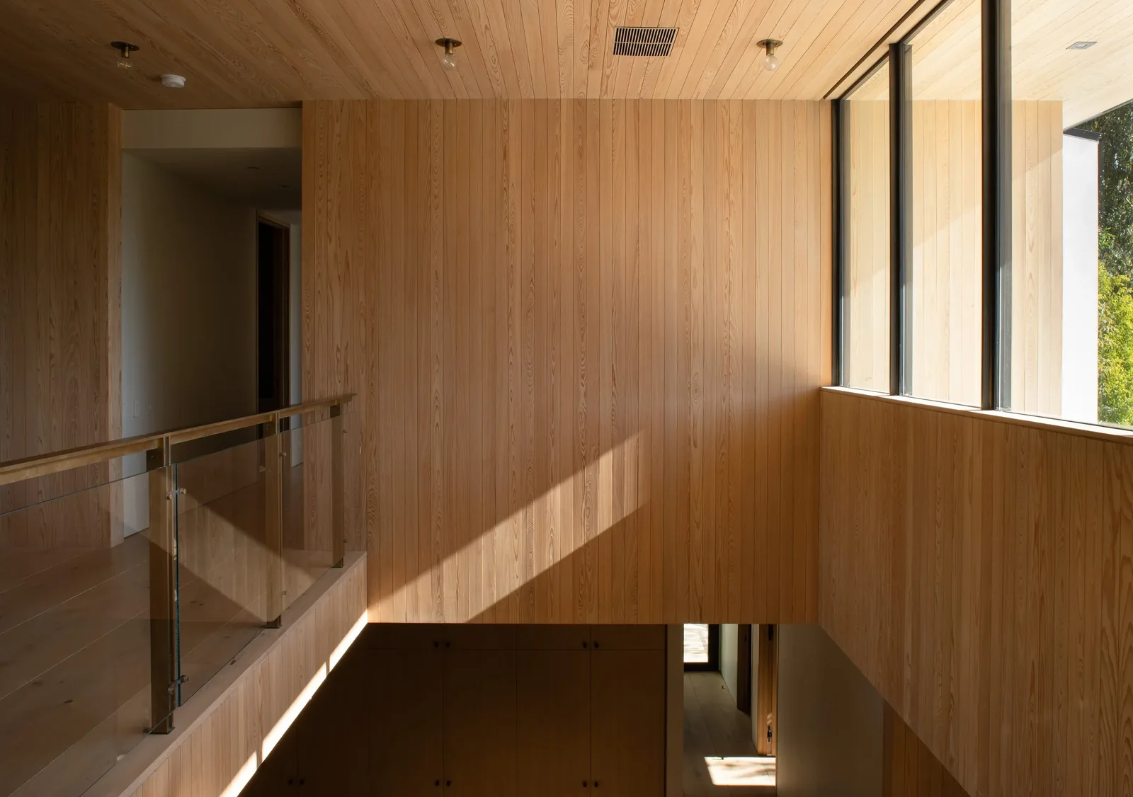 Hallway featuring wood paneling, glass railing, and large windows.