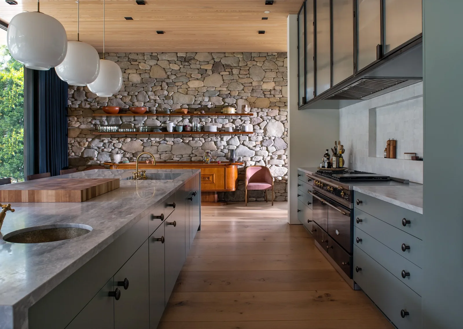 Kitchen featuring a stone accent wall with open wooden shelves, gray cabinets, and a large island with pendant lighting.