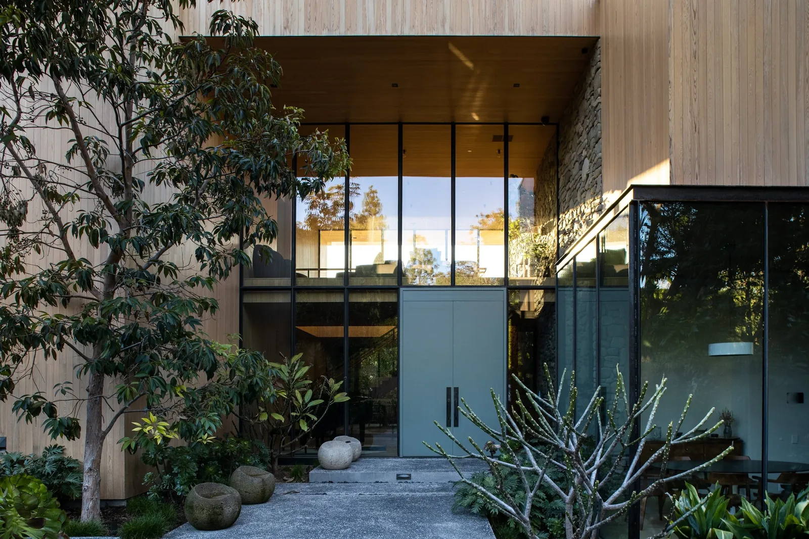 Front exterior view of a modern home with large glass windows, wood siding, and a landscaped entry path.